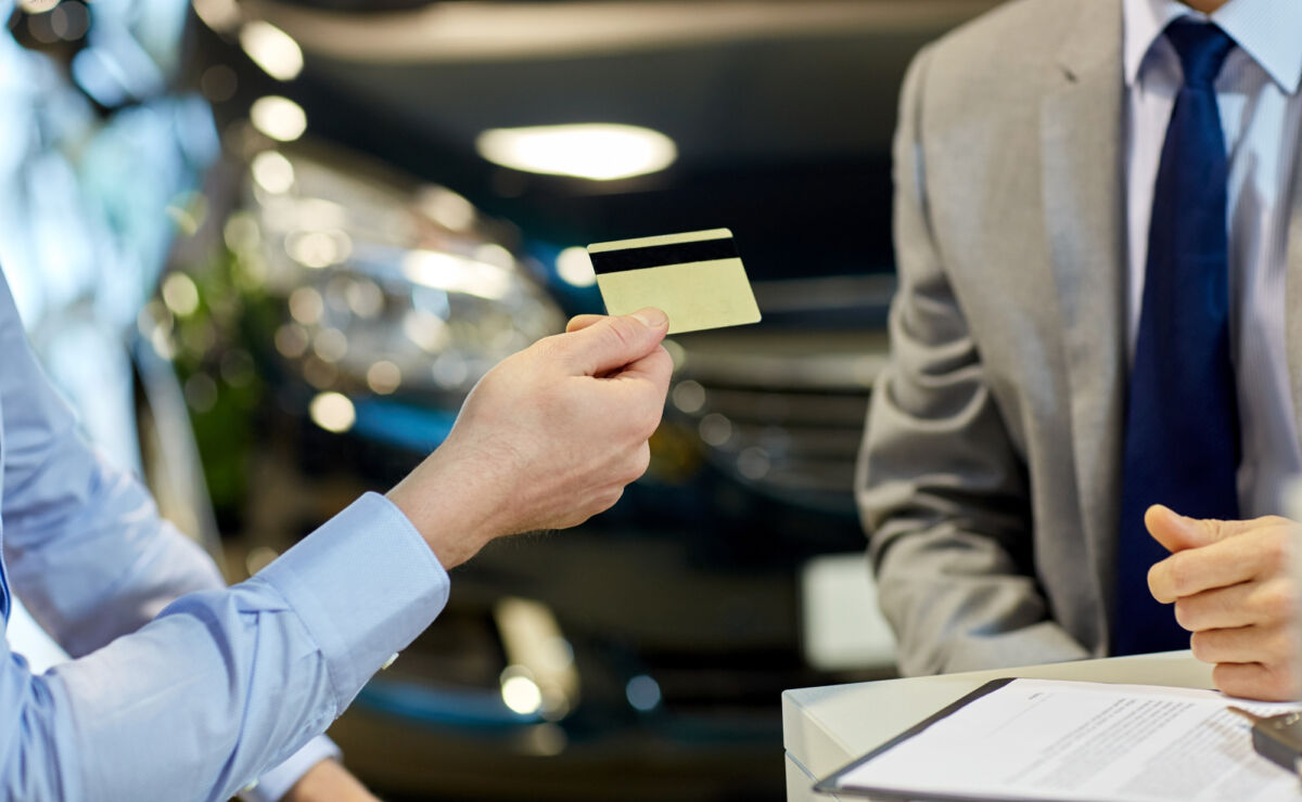 auto business, sale and people concept - close up of customer giving credit card to car dealer in auto show or salon