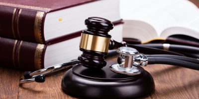 Brown Gavel With Medical Stethoscope Near Book At Wooden Desk In Courtroom