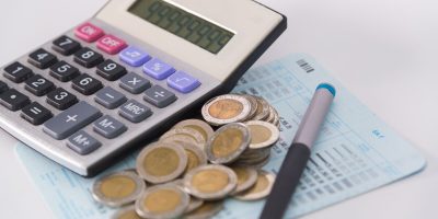 Savings, increasing columns of coins, piles of coins arranged as a graph and calculator with pen on white background, business idea, shallow focus.