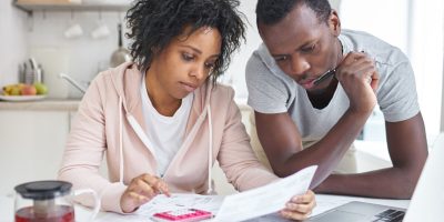 Young african american couple doing paperwork together, planning family budget, calculating domestic expenses, sitting at kitchen table with laptop and calculator at home. Financial problems concept