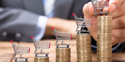 Midsection of businessman placing shopping cart on stacked coins in increasing order