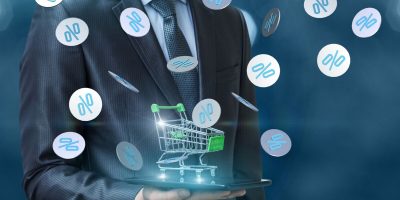Discounts in the online store. Businessman with shopping cart and percentages fly.