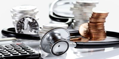 Financial health concept, stethoscope weaving around stacks of silver and gold coins and calculator