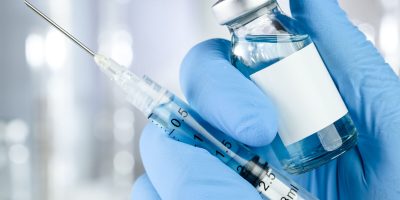 Healthcare concept with a hand in blue medical gloves holding a vaccine vial with blue liquid and black white label