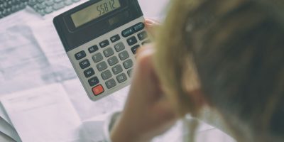 Woman uses a calculator to sum up expenses and holds her head worrying about the amount of money spent