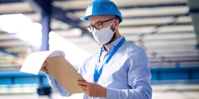 Man technician or engineer with protective mask and helmet working in industrial factory or warehouse.