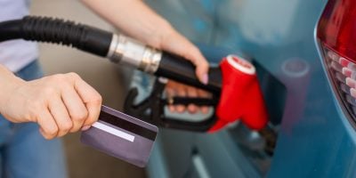 A woman fills her car with gasoline at a self-service gas station and holds a credit card.