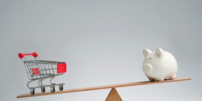 Shopping trolley and piggy bank balancing on a seesaw