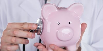 Cropped image of male doctor examining piggybank with stethoscope
