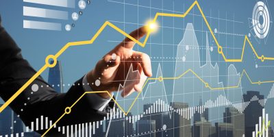 Close up of businessman finger pointing at creative business graph hologram on blurry city grid background. Finance, income and analysis concept. Double exposure