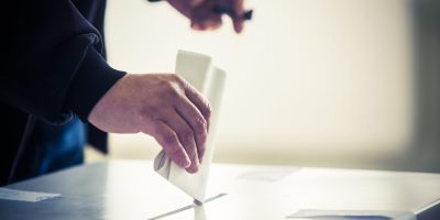 Hand of a person casting a ballot at a polling station during voting.