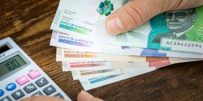 Man holds Colombian pesos in hand and counts on expenses or earnings calculator, Financial concept, home budget of Colombians