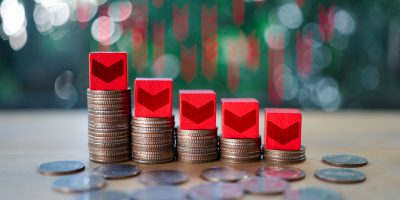 The down arrow on red wooden blocks on the graph of coins. Low interest in mortgages. Reducing interest payments for deposits. Concept of changing prices on the market