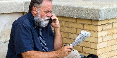 Mature unemployed salesman makes a call on his cell phone to reply to a advertisement for a want ad job in the newspaper.