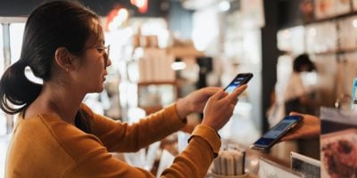Asian woman customer scanning smartphone to pay at coffee shop counter. Real lifestyle moment for fintech advertising, digital banking apps, QR payment. secure payment messaging, retail technology,